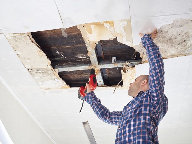 A handyman drilling into the roof through the ceiling